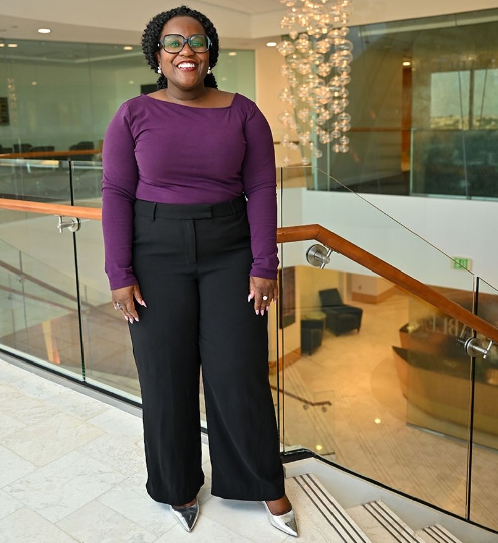 DMV Personal Stylist Letam Duson standing on steps wearing purple top, blacks slacks, and metallic silver heels.